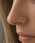 Close-up of a woman's face wearing a tiny gold heart stud nose ring on her left nostril.