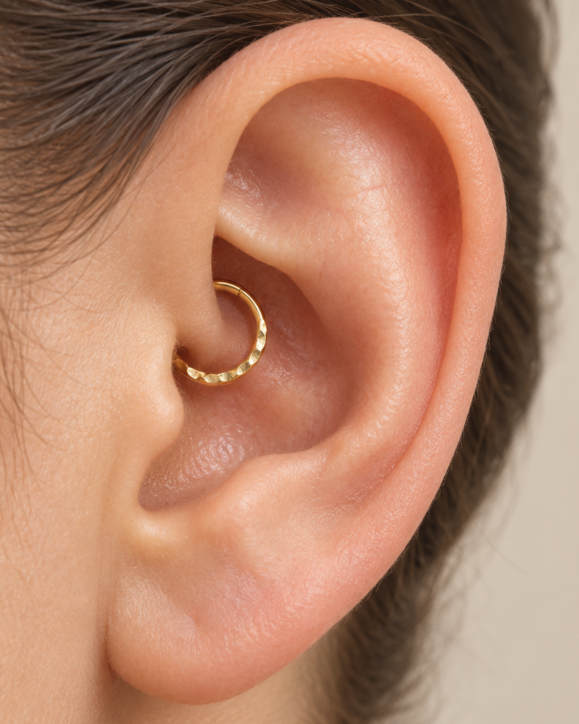 A small detail, tucked inside your ear. Ember brings a softly textured lower curve to a delicate 14ct solid gold daith ring. Its hand-hammered surface catches little flashes of light, while the upper arc stays smooth and polished.

We shape and hammer every ring individually, leaving a naturally uneven pattern that belongs to that piece alone. Choose a 6–10mm inner diameter, 18G or 20G, and yellow, white or rose gold. Handmade to order for fully healed daith piercings, with smooth round wire on both sides o