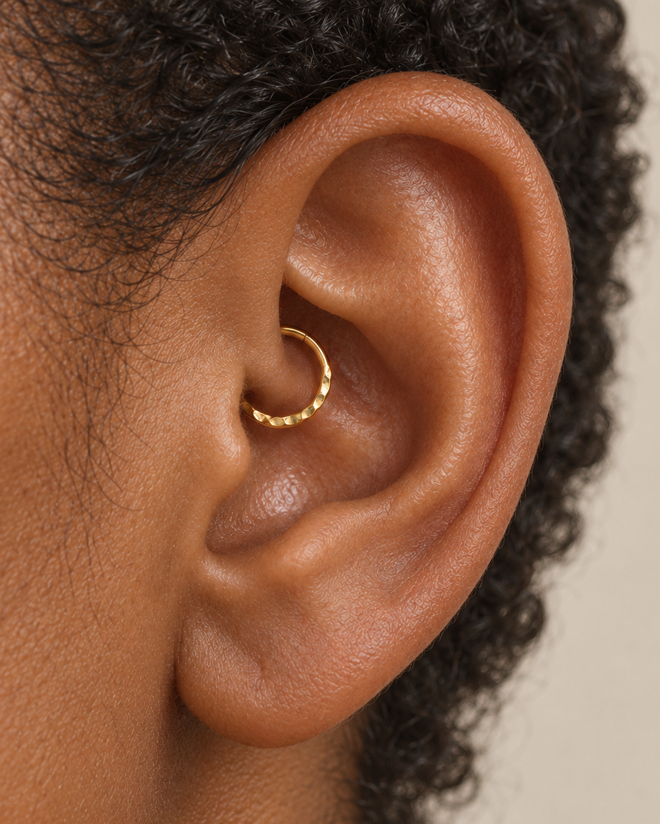 A small detail, tucked inside your ear. Ember brings a softly textured lower curve to a delicate 14ct solid gold daith ring. Its hand-hammered surface catches little flashes of light, while the upper arc stays smooth and polished.

We shape and hammer every ring individually, leaving a naturally uneven pattern that belongs to that piece alone. Choose a 6–10mm inner diameter, 18G or 20G, and yellow, white or rose gold. Handmade to order for fully healed daith piercings, with smooth round wire on both sides o