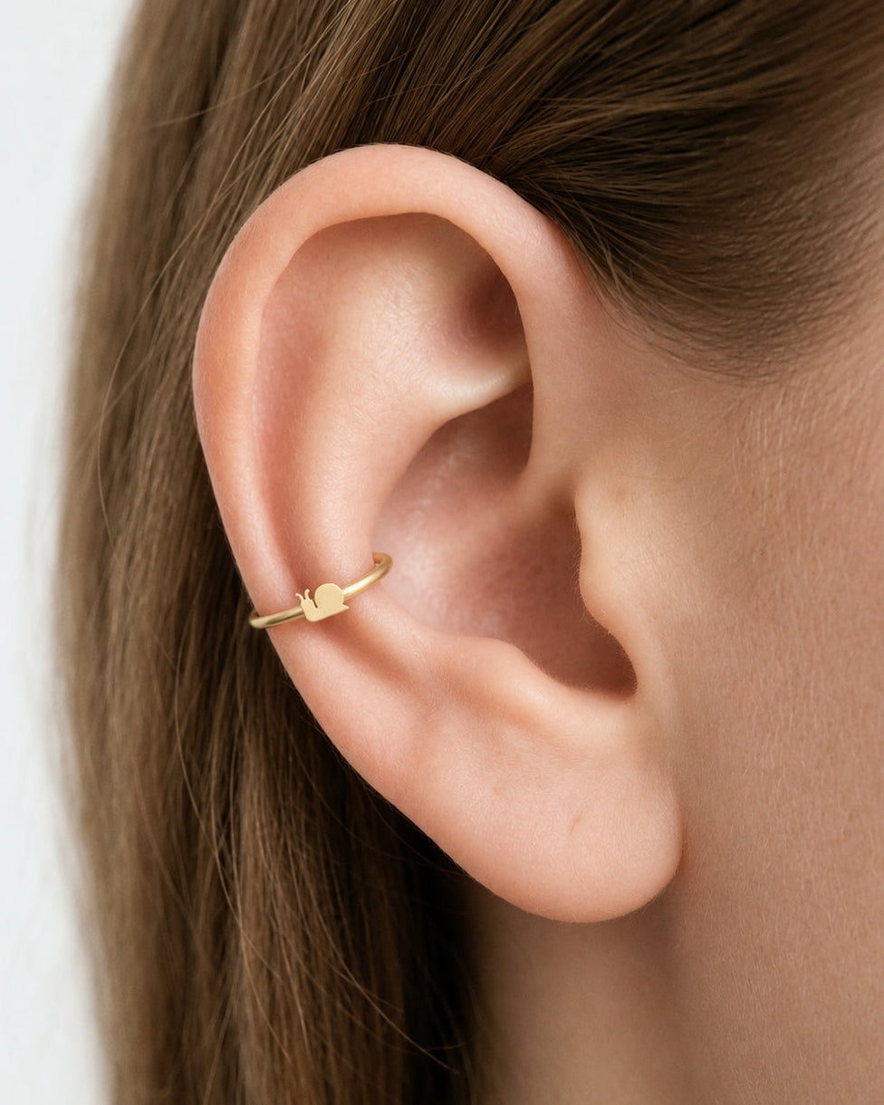 This miniature snail is shown in profile, with two upward-curving feelers, a rounded shell and a small tapered tail. Its smooth, polished surface has no engraved shell spiral or gemstones, keeping the silhouette clear and minimal.