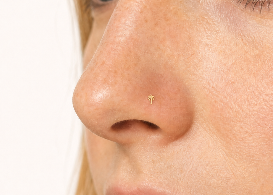 Close-up of a woman's face wearing a tiny gold nose pin on her left nostril, set against a clean white background.