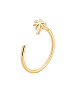 A gold open-ended  nose ring featuring a small palm tree charm at the top, photographed on a clean, light cream background.