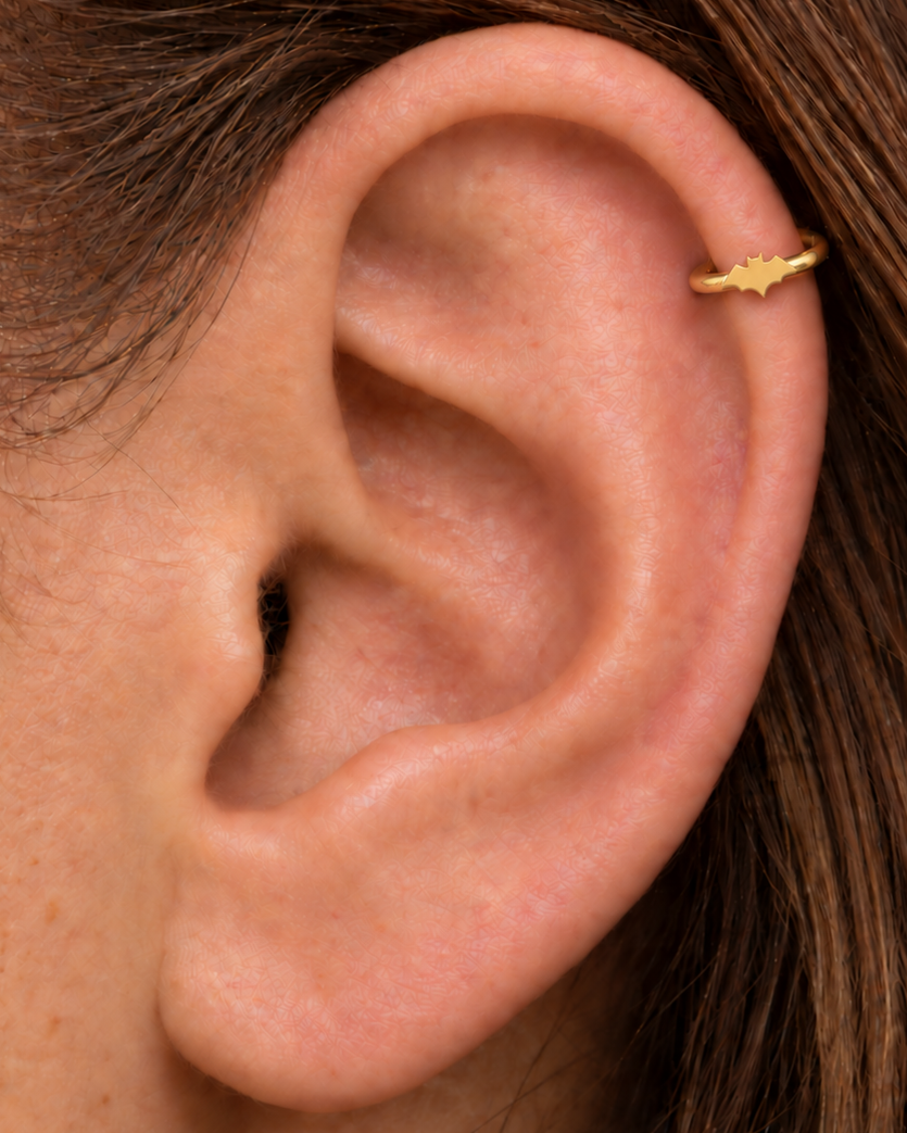 A small bat silhouette gives the hoop a sharper Halloween edge that can also work with gothic styling. Made for fully healed helix piercings, it keeps the profile compact for an upper-ear stack while leaving the motif clearly visible. Handmade to order in 14ct solid gold, it fits naturally with spooky, gothic and Halloween-led styling rather than reading as a generic plain hoop.
