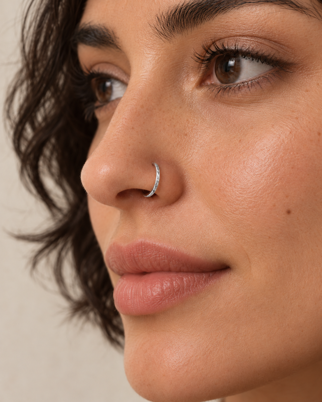 A little light beside your smile. Luma brings a softly shifting glow to a delicate 14ct solid gold nostril ring. The entire outer circumference is hammered by hand with tiny, irregular transverse marks: short strokes across the outer edge that catch the light in little flashes. The front-facing side and inner surface remain smooth and polished.

The width, depth, angle and spacing of these small marks vary naturally with each hammer stroke. No two rings have exactly the same pattern; yours will share the de