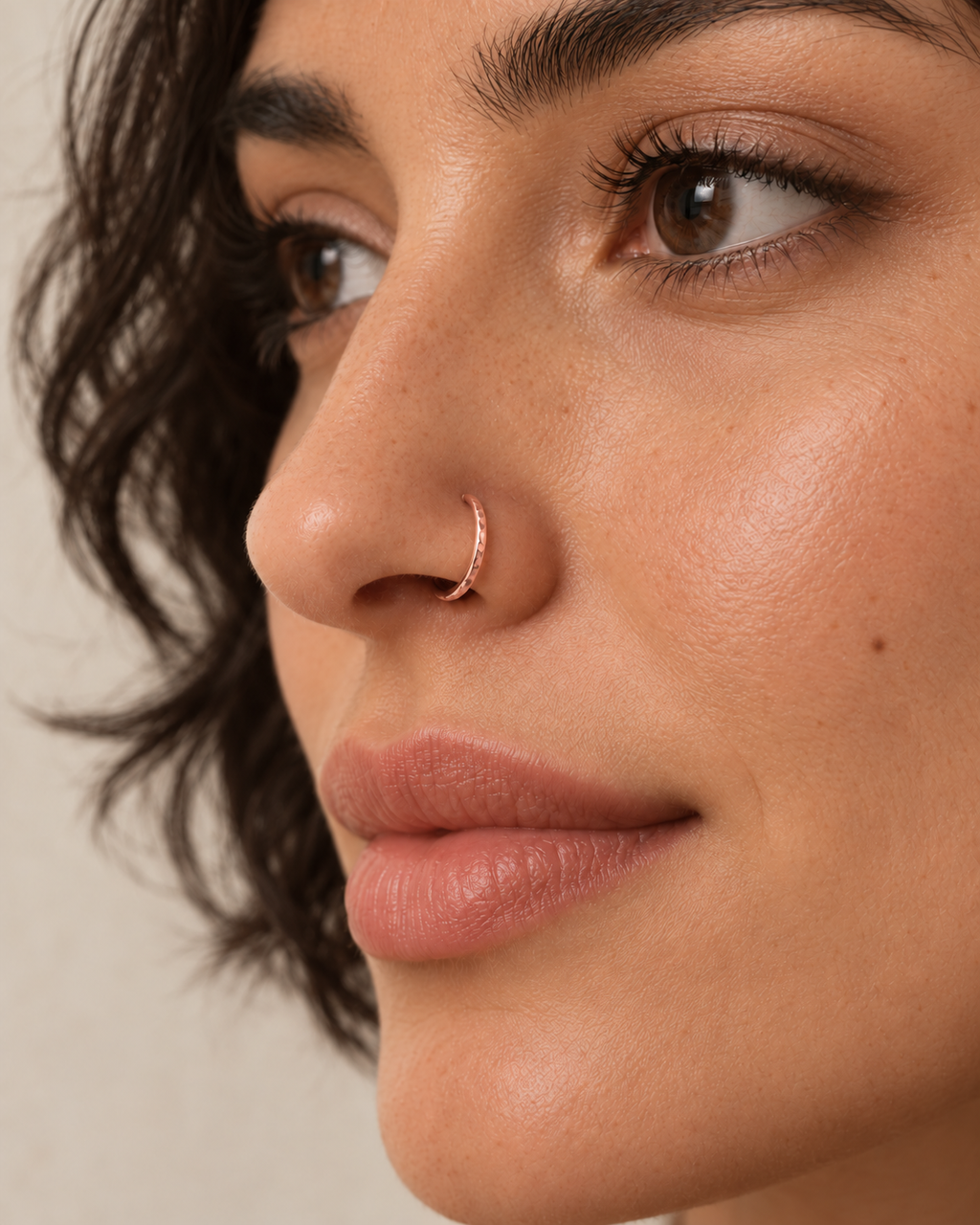 A little light beside your smile. Luma brings a softly shifting glow to a delicate 14ct solid gold nostril ring. The entire outer circumference is hammered by hand with tiny, irregular transverse marks: short strokes across the outer edge that catch the light in little flashes. The front-facing side and inner surface remain smooth and polished.

The width, depth, angle and spacing of these small marks vary naturally with each hammer stroke. No two rings have exactly the same pattern; yours will share the de