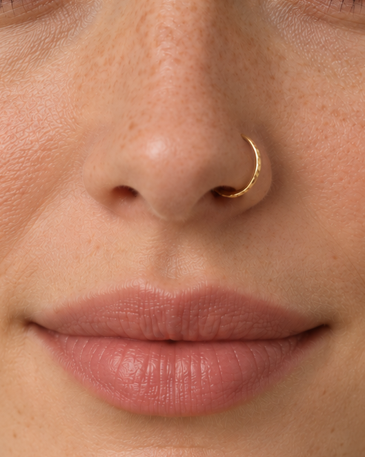 A little light beside your smile. Luma brings a softly shifting glow to a delicate 14ct solid gold nostril ring. The entire outer circumference is hammered by hand with tiny, irregular transverse marks: short strokes across the outer edge that catch the light in little flashes. The front-facing side and inner surface remain smooth and polished.

The width, depth, angle and spacing of these small marks vary naturally with each hammer stroke. No two rings have exactly the same pattern; yours will share the de
