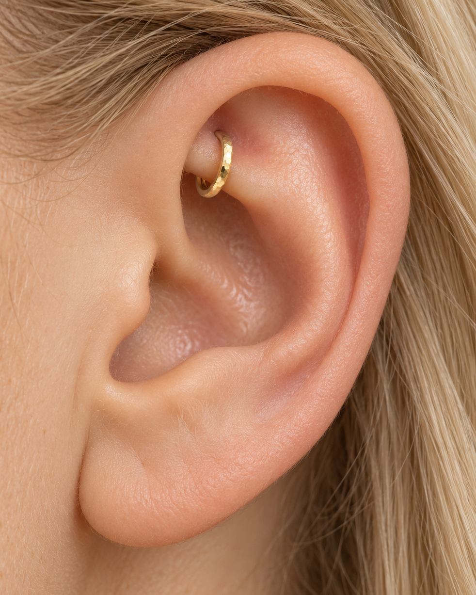 A quiet flash of gold in the upper fold of your ear. Luma brings a softly shifting glow to a delicate 14ct solid gold rook ring. The entire outer circumference is hammered by hand with tiny, irregular transverse marks: short strokes across the outer edge that catch the light in little flashes. The front-facing side and inner surface remain smooth and polished.