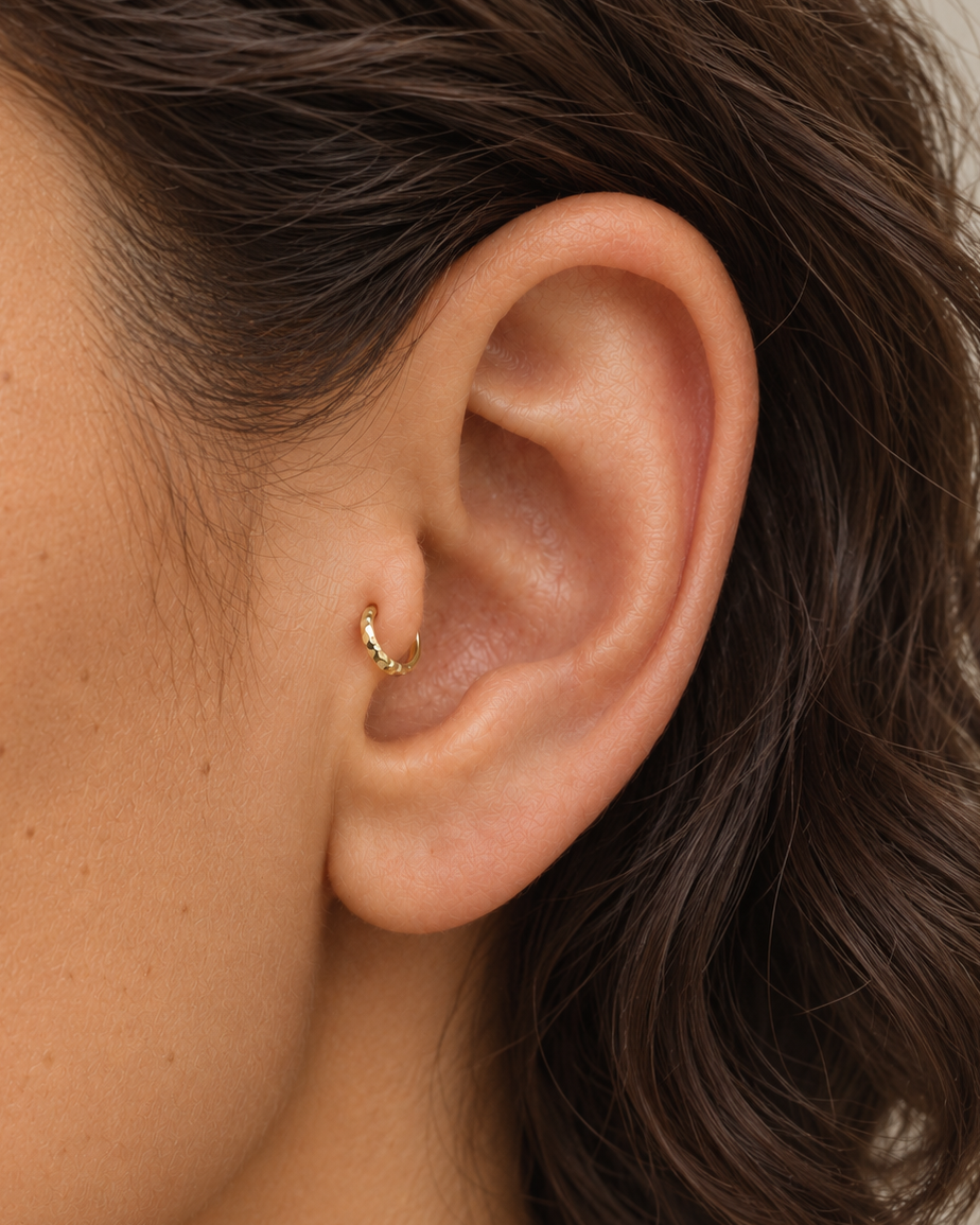 A tiny detail with a little light of its own. Luma brings a softly shifting glow to a delicate 14ct solid gold tragus ring. The entire outer circumference is hammered by hand with tiny, irregular transverse marks: short strokes across the outer edge that catch the light in little flashes. The front-facing side and inner surface remain smooth and polished.

The width, depth, angle and spacing of these small marks vary naturally with each hammer stroke. No two rings have exactly the same pattern; yours will s