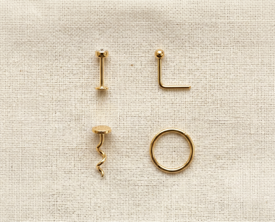 Nostril piercing jewellery types compared: flat-back labret stud, L-shape stud, corkscrew, and 14K gold seamless hoop