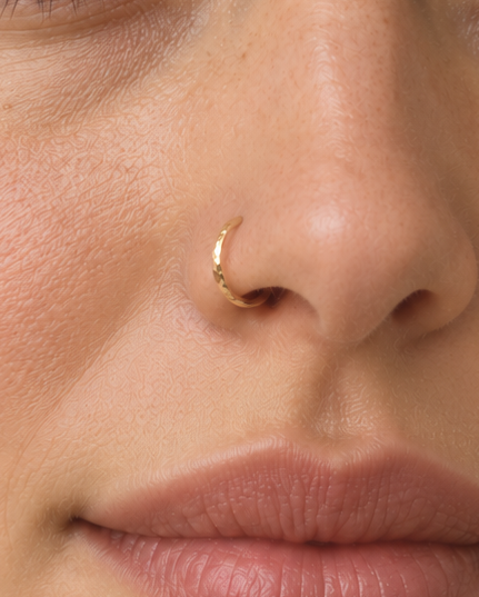 A delicate 14ct solid gold nose hoop with a widening hand-hammered detail. Handmade to order in your choice of diameter, gauge and yellow, white or rose gold.