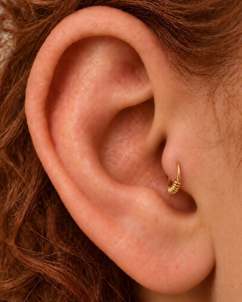 A small detail at the front of your ear. Solis brings a softly wrapped lower curve to a delicate 14ct solid gold tragus ring. Fine gold wire is wound by hand around approximately half the hoop, while the upper arc stays smooth and polished.
