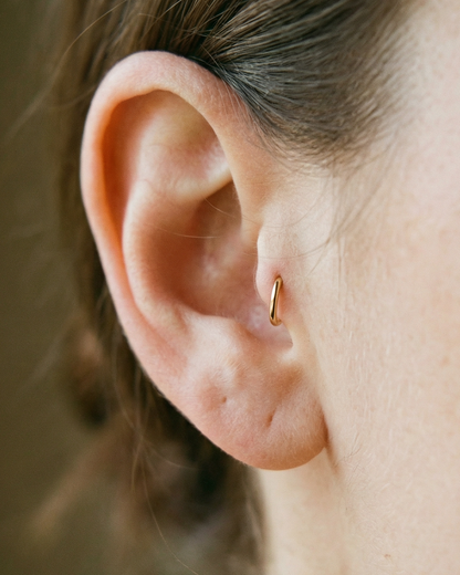 Close-up of an ear with a gold hoop earring against a blurred background