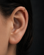 Close-up of an ear wearing a gold earring against a dark background