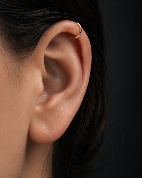 Close-up of an ear wearing a gold earring against a dark background — 14K solid gold by Stepoy