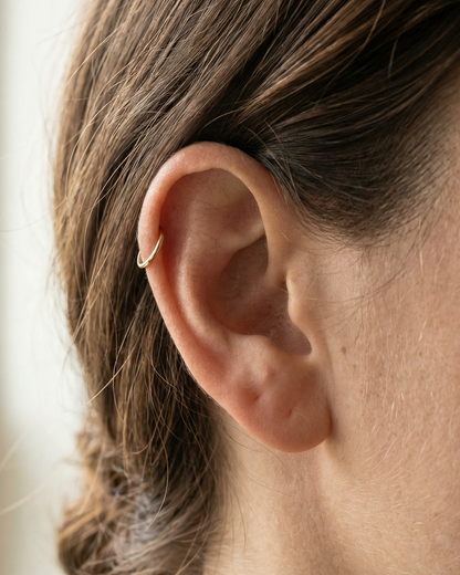 Close-up of a person's ear with a gold earring, blurred background