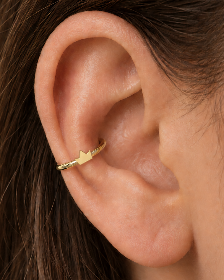 A tiny crown adds a playful statement detail while staying compact enough for everyday styling. Made for fully healed conch piercings, it pairs the larger hoop silhouette of a conch ring with a small fixed motif for a more distinctive ear stack. Handmade to order in 14ct solid gold, it fits naturally with playful, symbolic and statement-led styling rather than reading as a generic plain hoop.