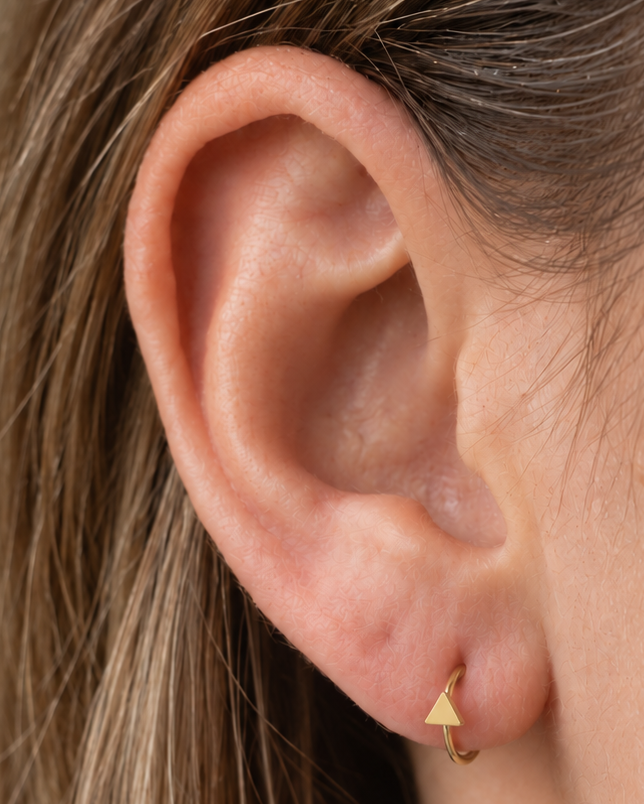 A small triangle gives the hoop a sharper geometric detail with a clean modern feel. Made for fully healed lobe piercings and sold individually, it works easily in first, second or third-lobe stacks. Handmade to order in 14ct solid gold, it fits naturally with clean, geometric and modern styling rather than reading as a generic plain hoop.