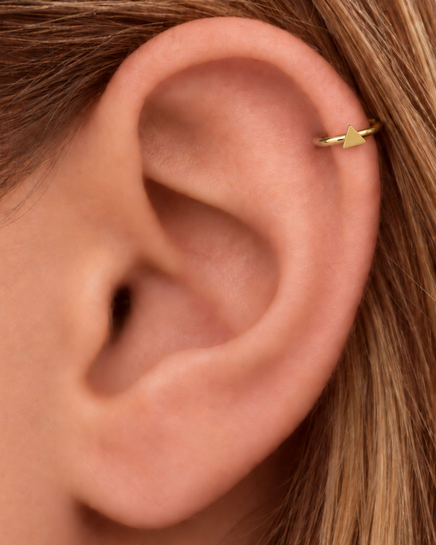 A small triangle gives the hoop a sharper geometric detail with a clean modern feel. Made for fully healed helix piercings, it keeps the profile compact for an upper-ear stack while leaving the motif clearly visible. Handmade to order in 14ct solid gold, it fits naturally with clean, geometric and modern styling rather than reading as a generic plain hoop.