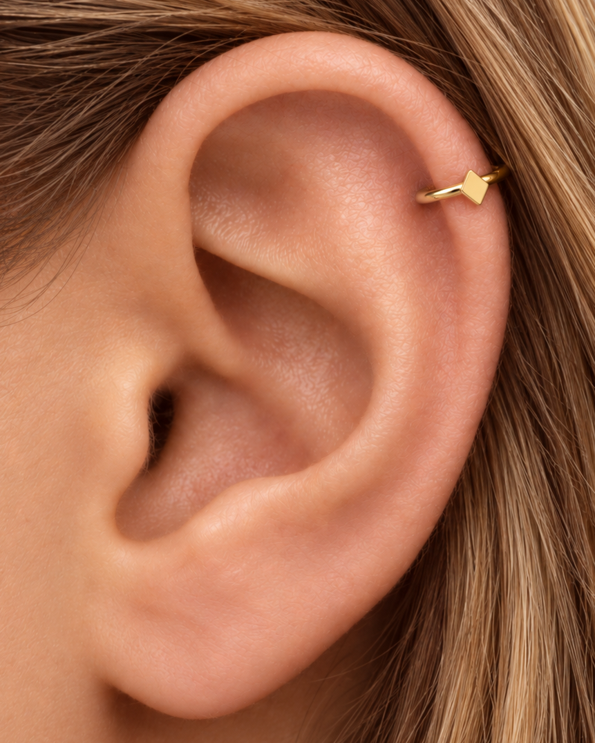 A diamond-shaped motif brings a neat angular detail without using stones or settings. Made for fully healed helix piercings, it keeps the profile compact for an upper-ear stack while leaving the motif clearly visible. Handmade to order in 14ct solid gold, it fits naturally with angular, geometric and polished styling rather than reading as a generic plain hoop.