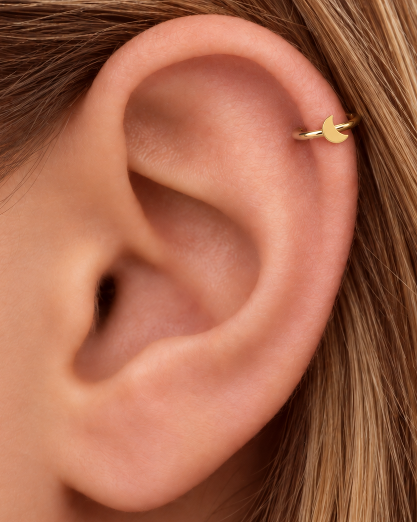 A small crescent moon gives the hoop a subtle celestial character with a polished solid-gold finish. Made for fully healed helix piercings, it keeps the profile compact for an upper-ear stack while leaving the motif clearly visible. Handmade to order in 14ct solid gold, it fits naturally with celestial, lunar and softly symbolic styling rather than reading as a generic plain hoop.