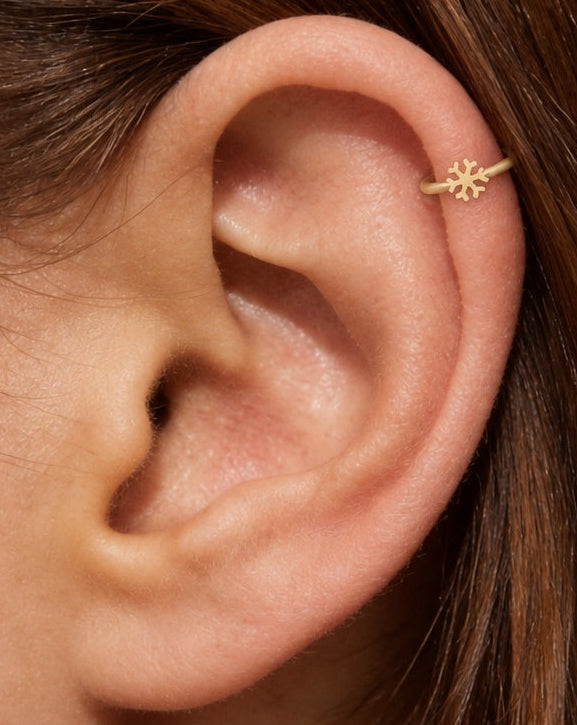 This miniature snowflake has six arms radiating from a solid centre, each with small branches and rounded ends. The spaces between the arms define the shape, while the smooth gold surface keeps the design simple. There are no gemstones or engraved details.

Handmade to order in nickel-free 14ct solid gold, this snowflake helix hoop is available in yellow, white or rose gold. Choose a 5, 6 or 7mm internal diameter and 18G (1.0mm) or 20G (0.8mm). The motif measures approximately 3mm. Designed for fully healed