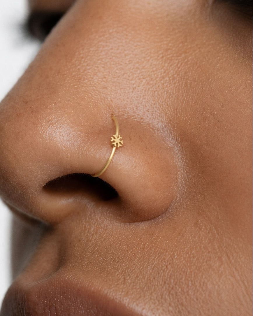 This miniature snowflake has six arms radiating from a solid centre, each with small branches and rounded ends. The spaces between the arms define the shape, while the smooth gold surface keeps the design simple. There are no gemstones or engraved details.

Handmade to order in nickel-free 14ct solid gold, this snowflake nostril hoop is available in yellow, white or rose gold. Choose a 6, 7, 8, 9 or 10mm internal diameter and 18G (1.0mm) or 20G (0.8mm). The motif measures approximately 3mm. Designed for ful