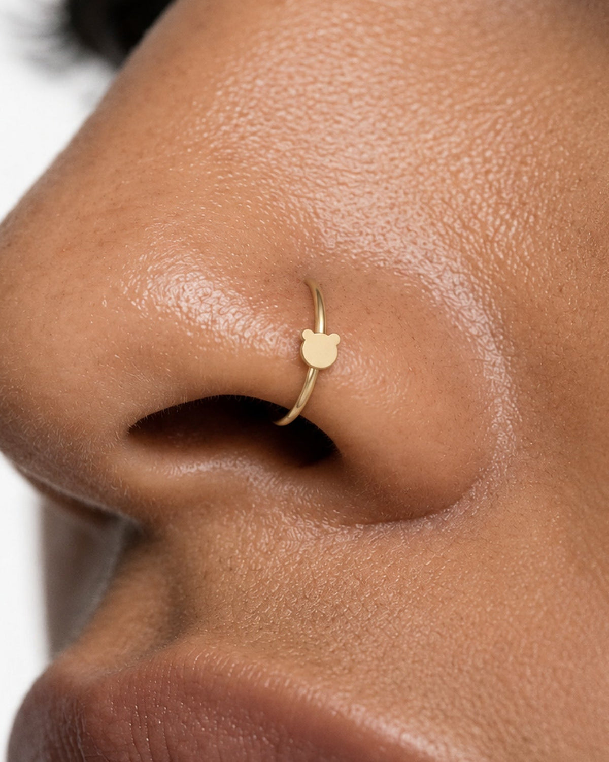 Two round ears, one familiar little face. This 14ct solid gold bear nostril ring pairs an approximately 3mm polished bear-head silhouette with a smooth seamless hoop. Its rounded outline gives the design a playful teddy-bear feel, with no engraved facial features or gemstones.
Handmade to order in yellow, white or rose gold, with inner diameters from 6 to 10mm and a choice of 18G (1.0mm) or 20G (0.8mm). Both the bear motif and hoop are solid gold and nickel-free, designed for a fully healed nostril piercing