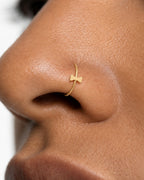 This miniature bow tie has two flared sides joined by a small central knot. Rounded outer corners soften its geometric outline, while the smooth gold surface keeps the design minimal. There are no trailing ribbon ends, engraved details or gemstones.

Handmade to order in nickel-free 14ct solid gold, this bow tie nostril hoop is available in yellow, white or rose gold. Choose a 6, 7, 8, 9 or 10mm internal diameter and 18G (1.0mm) or 20G (0.8mm). The motif measures approximately 3mm. Designed for fully healed