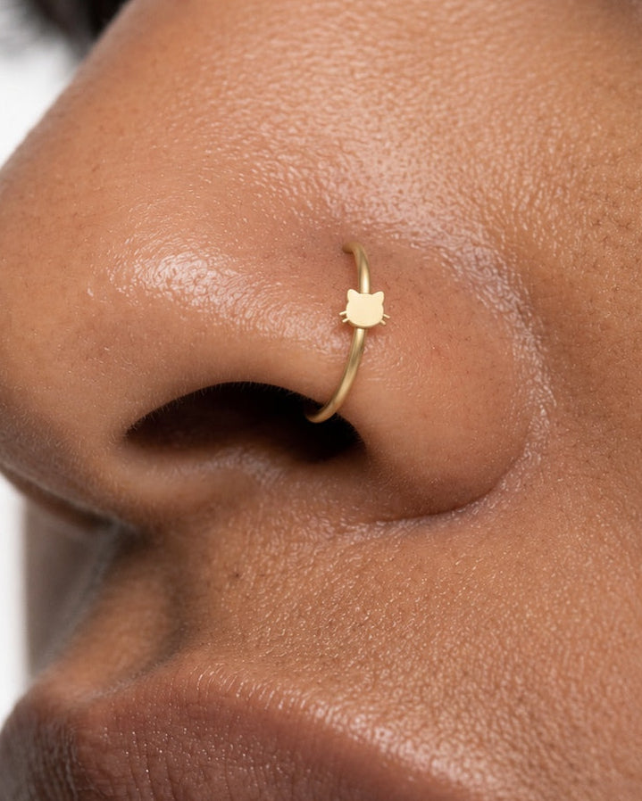 Two little ears and a few whiskers give this hoop its feline character. This 14ct solid gold cat head nostril ring pairs an approximately 3mm polished cat-face silhouette with a smooth seamless hoop. The rounded face is left plain, allowing the ears and whiskers to define the design.
Handmade to order in yellow, white or rose gold, with inner diameters from 6 to 10mm and a choice of 18G (1.0mm) or 20G (0.8mm). Both the cat head and hoop are solid gold and nickel-free, designed for a fully healed nostril pie