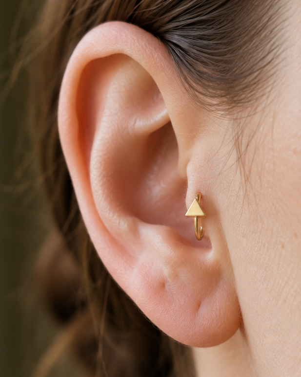 A small triangle gives the hoop a sharper geometric detail with a clean modern feel. Made for fully healed tragus piercings, it adds a compact decorative detail without turning the piece into a dangling design. Handmade to order in 14ct solid gold, it fits naturally with clean, geometric and modern styling rather than reading as a generic plain hoop.