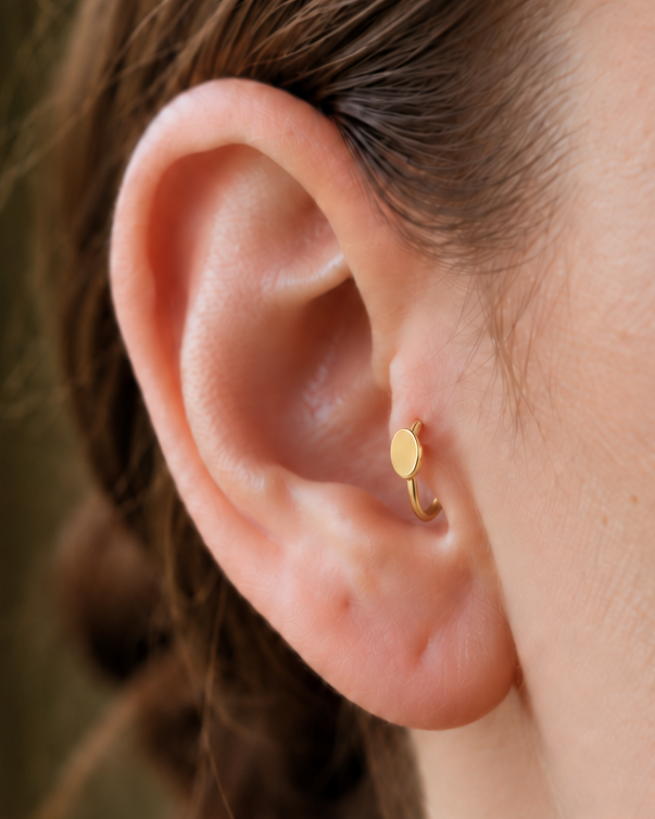A polished oval adds a softer geometric detail for a clean, understated look. Made for fully healed tragus piercings, it adds a compact decorative detail without turning the piece into a dangling design. Handmade to order in 14ct solid gold, it fits naturally with softly geometric and minimal styling rather than reading as a generic plain hoop.