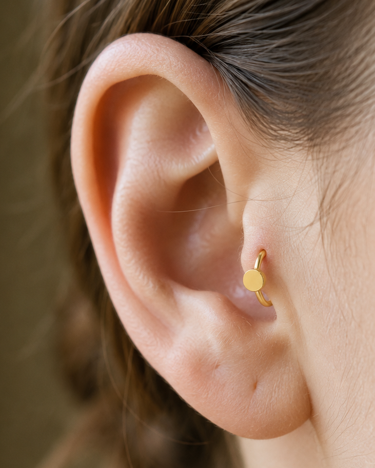 A simple circle motif keeps the design pared back, rounded and easy to mix with other jewellery. Made for fully healed tragus piercings, it adds a compact decorative detail without turning the piece into a dangling design. Handmade to order in 14ct solid gold, it fits naturally with simple, rounded and minimal styling rather than reading as a generic plain hoop.