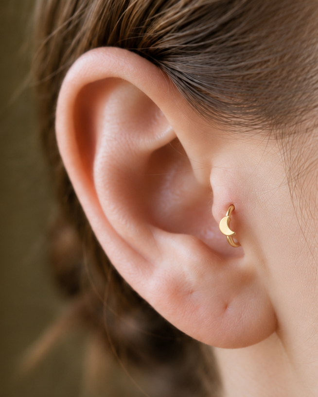A small crescent moon gives the hoop a subtle celestial character with a polished solid-gold finish. Made for fully healed tragus piercings, it adds a compact decorative detail without turning the piece into a dangling design. Handmade to order in 14ct solid gold, it fits naturally with celestial, lunar and softly symbolic styling rather than reading as a generic plain hoop.