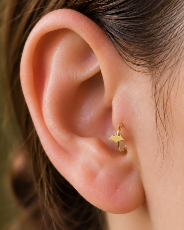 A small bat silhouette gives the hoop a sharper Halloween edge that can also work with gothic styling. Made for fully healed tragus piercings, it adds a compact decorative detail without turning the piece into a dangling design. Handmade to order in 14ct solid gold, it fits naturally with spooky, gothic and Halloween-led styling rather than reading as a generic plain hoop.