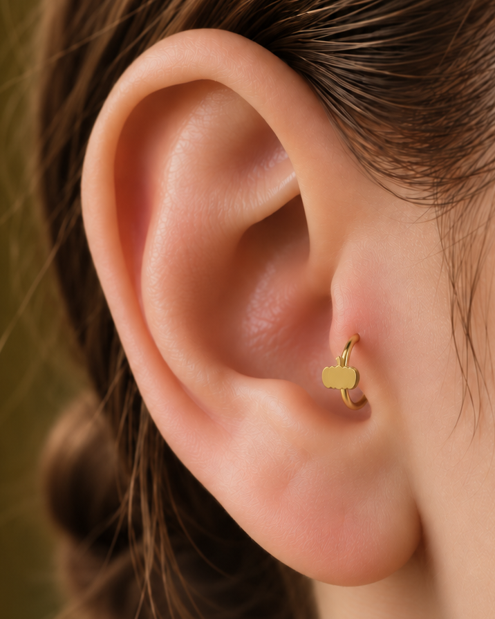 A tiny pumpkin adds an autumn and Halloween note while keeping the piece polished and wearable. Made for fully healed tragus piercings, it adds a compact decorative detail without turning the piece into a dangling design. Handmade to order in 14ct solid gold, it fits naturally with autumnal, festive and Halloween-led styling rather than reading as a generic plain hoop.