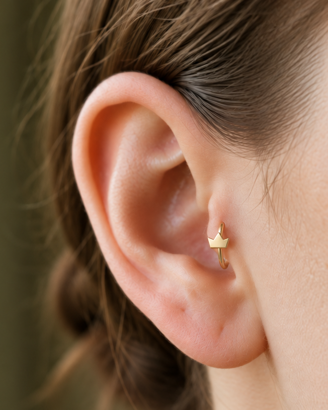 A tiny crown adds a playful statement detail while staying compact enough for everyday styling. Made for fully healed tragus piercings, it adds a compact decorative detail without turning the piece into a dangling design. Handmade to order in 14ct solid gold, it fits naturally with playful, symbolic and statement-led styling rather than reading as a generic plain hoop.