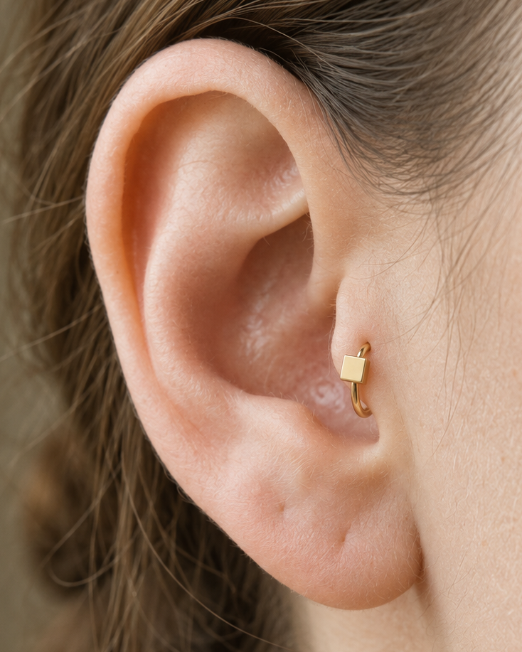 A small square motif gives the hoop a crisp, graphic finish while keeping the overall design minimal. Made for fully healed tragus piercings, it adds a compact decorative detail without turning the piece into a dangling design. Handmade to order in 14ct solid gold, it fits naturally with crisp, geometric and minimal styling rather than reading as a generic plain hoop.