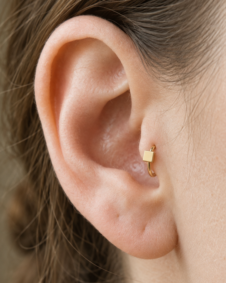 A small square motif gives the hoop a crisp, graphic finish while keeping the overall design minimal. Made for fully healed tragus piercings, it adds a compact decorative detail without turning the piece into a dangling design. Handmade to order in 14ct solid gold, it fits naturally with crisp, geometric and minimal styling rather than reading as a generic plain hoop.