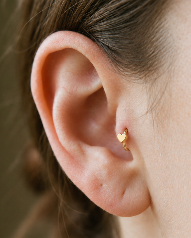 A softly rounded heart adds a sweet, personal detail to a simple gold hoop. Made for fully healed tragus piercings, it adds a compact decorative detail without turning the piece into a dangling design. Handmade to order in 14ct solid gold, it fits naturally with soft, personal and romantic styling rather than reading as a generic plain hoop.