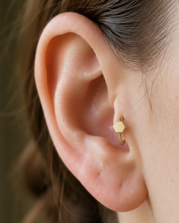 A polished hexagon adds a structured geometric accent that still feels easy to wear. Made for fully healed tragus piercings, it adds a compact decorative detail without turning the piece into a dangling design. Handmade to order in 14ct solid gold, it fits naturally with structured, geometric and modern styling rather than reading as a generic plain hoop.