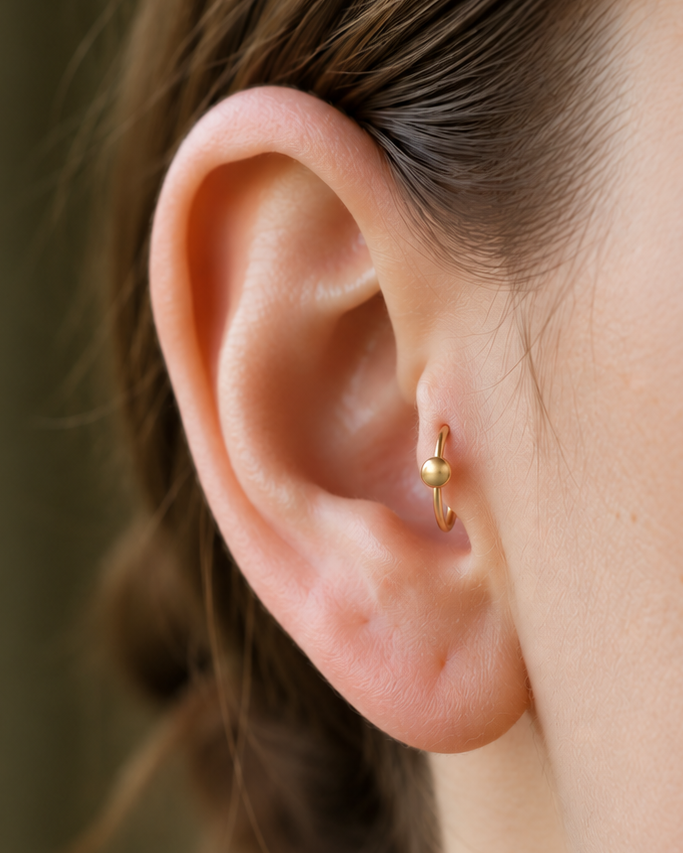 A polished gold ball adds a classic bead-like detail that works easily with simple solid-gold jewellery. Made for fully healed tragus piercings, it adds a compact decorative detail without turning the piece into a dangling design. Handmade to order in 14ct solid gold, it fits naturally with classic, polished and minimal styling rather than reading as a generic plain hoop.
