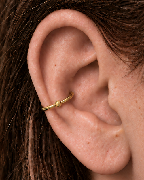 A polished gold ball adds a classic bead-like detail that works easily with simple solid-gold jewellery. Made for fully healed conch piercings, it pairs the larger hoop silhouette of a conch ring with a small fixed motif for a more distinctive ear stack. Handmade to order in 14ct solid gold, it fits naturally with classic, polished and minimal styling rather than reading as a generic plain hoop.