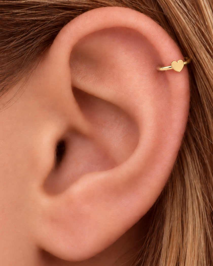 A softly rounded heart adds a sweet, personal detail to a simple gold hoop. Made for fully healed helix piercings, it keeps the profile compact for an upper-ear stack while leaving the motif clearly visible. Handmade to order in 14ct solid gold, it fits naturally with soft, personal and romantic styling rather than reading as a generic plain hoop.