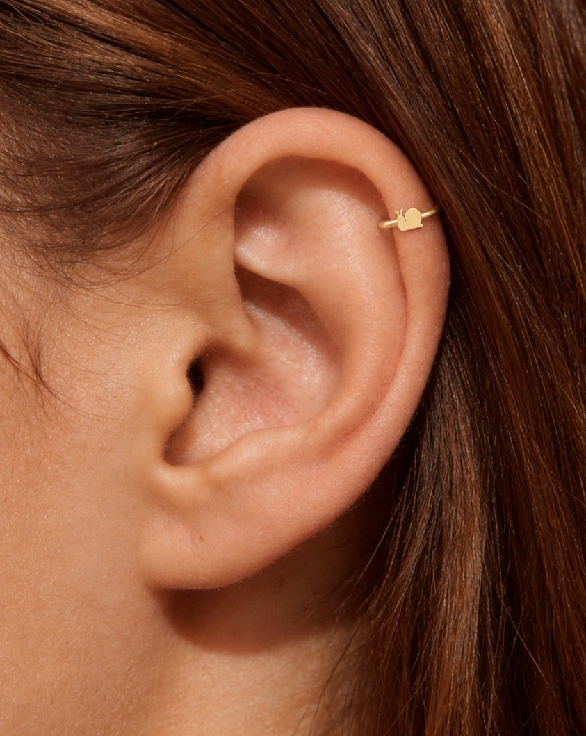 This miniature snail is shown in profile, with two upward-curving feelers, a rounded shell and a small tapered tail. Its smooth, polished surface has no engraved shell spiral or gemstones, keeping the silhouette clear and minimal.

Handmade to order in nickel-free 14ct solid gold, this snail helix hoop is available in yellow, white or rose gold. Choose a 5, 6 or 7mm internal diameter and 18G (1.0mm) or 20G (0.8mm). 