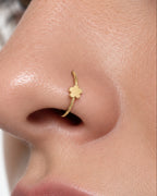 A close-up of a person's nose wearing a delicate gold nose ring with a small flower-shaped tip.