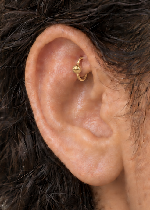 A polished ball adds a classic bead-like detail that works easily with simple solid-gold jewellery. Made for fully healed traditional rook piercings, it gives a small curved ear placement a clear motif-led detail while keeping the hoop clean and wearable. Handmade to order in 14ct solid gold, it fits naturally with classic, polished and minimal styling rather than reading as a generic plain hoop.