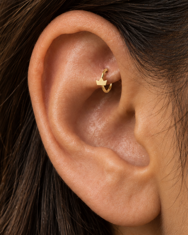 A tiny crown adds a playful statement detail while staying compact enough for everyday styling. Made for fully healed traditional rook piercings, it gives a small curved ear placement a clear motif-led detail while keeping the hoop clean and wearable. Handmade to order in 14ct solid gold, it fits naturally with playful, symbolic and statement-led styling rather than reading as a generic plain hoop.
