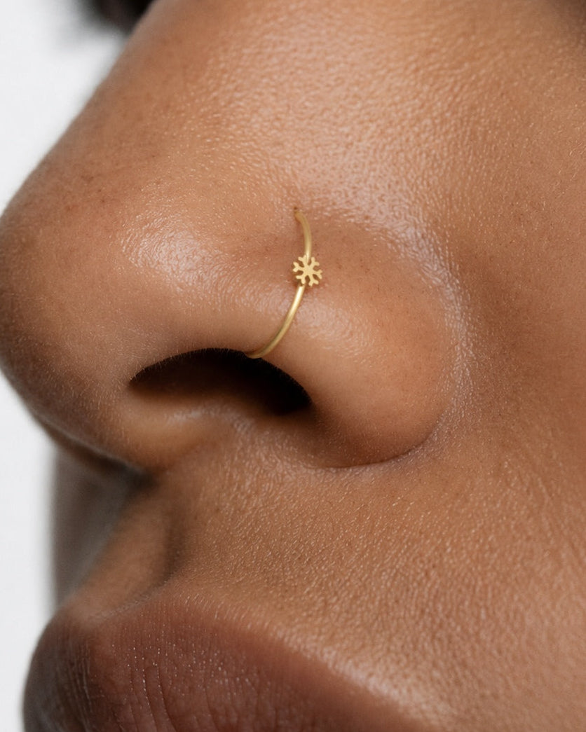 This miniature snowflake has six arms radiating from a solid centre, each with small branches and rounded ends. The spaces between the arms define the shape, while the smooth gold surface keeps the design simple. There are no gemstones or engraved details.

Handmade to order in nickel-free 14ct solid gold, this snowflake nostril hoop is available in yellow, white or rose gold. Choose a 6, 7, 8, 9 or 10mm internal diameter and 18G (1.0mm) or 20G (0.8mm). The motif measures approximately 3mm. Designed for ful
