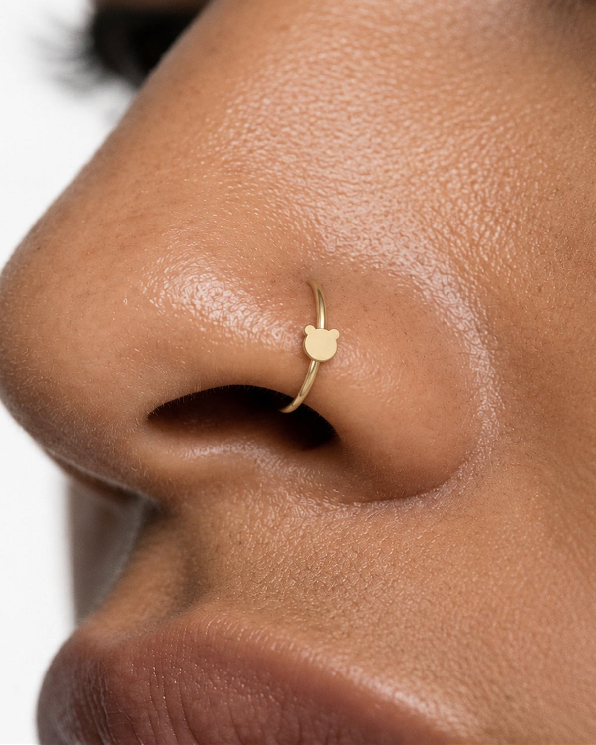 Two round ears, one familiar little face. This 14ct solid gold bear nostril ring pairs an approximately 3mm polished bear-head silhouette with a smooth seamless hoop. Its rounded outline gives the design a playful teddy-bear feel, with no engraved facial features or gemstones.
Handmade to order in yellow, white or rose gold, with inner diameters from 6 to 10mm and a choice of 18G (1.0mm) or 20G (0.8mm). Both the bear motif and hoop are solid gold and nickel-free, designed for a fully healed nostril piercing