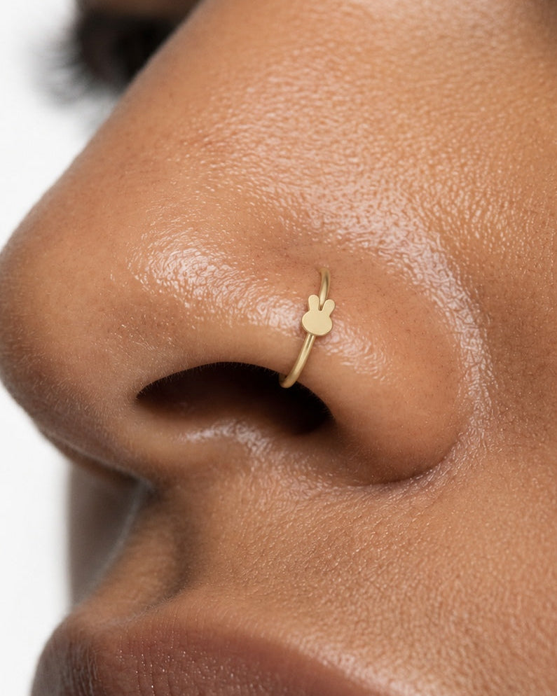 Two little ears, one playful detail. This 14ct solid gold rabbit nostril ring pairs an approximately 3mm polished bunny-head silhouette with a smooth seamless hoop. Upright ears with rounded tips and a softly curved face give the motif its character, with no engraved features or gemstones.
Handmade to order in yellow, white or rose gold, with inner diameters from 6 to 10mm and a choice of 18G (1.0mm) or 20G (0.8mm). Both the rabbit motif and hoop are solid gold and nickel-free, designed for a fully healed n